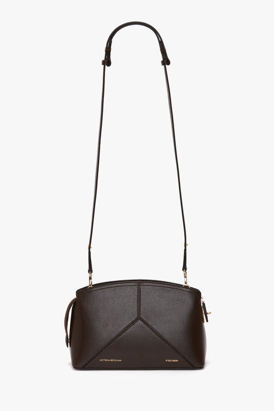 Introducing the Exclusive Victoria Crossbody Bag In Brown Leather by Victoria Beckham, a structured dark brown calf leather shoulder bag with an adjustable strap and gold hardware. It features a signature V shape and small gold text near the bottom, adding a touch of elegance to its geometric design.