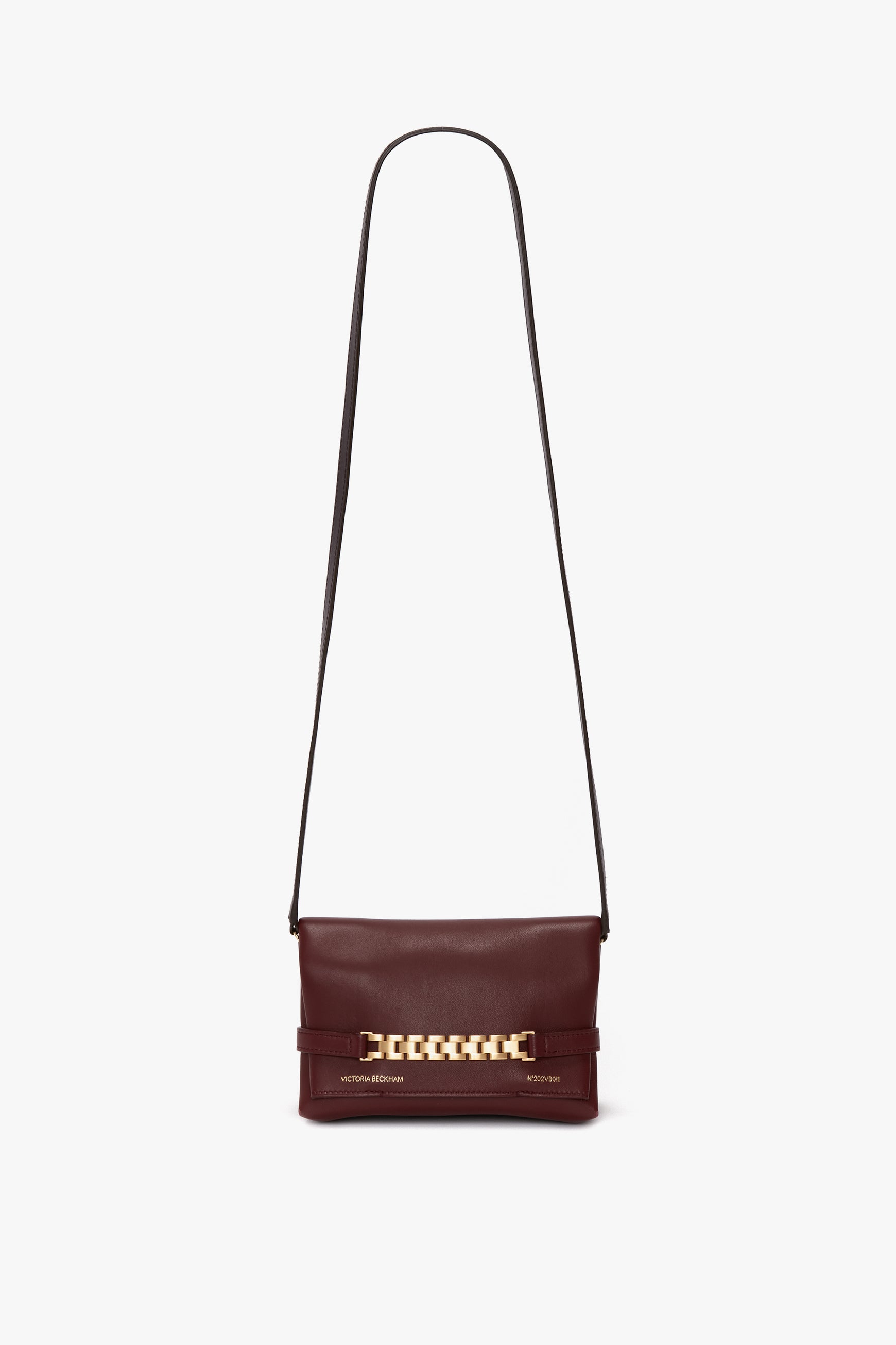 A small, burgundy leather bag featuring a gold chain accent on the front flap and a detachable strap for versatile wear. This is the Mini Chain With Long Strap Pouch Bag In Burgundy Leather by Victoria Beckham.