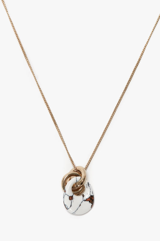 Victoria Beckham Exclusive Resin Pendant Necklace In Light Gold-White with a white, marbled resin pendant intertwined with three small gold rings and a T-bar closure.