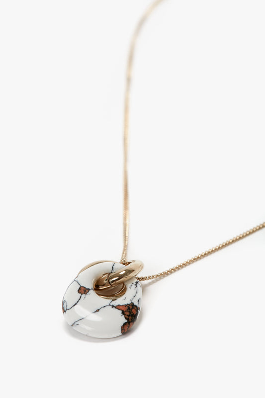 A Victoria Beckham Exclusive Resin Pendant Necklace In Light Gold-White with a round white resin pendant featuring black and brown veining, complemented by a secure T-bar closure, against a plain white background.