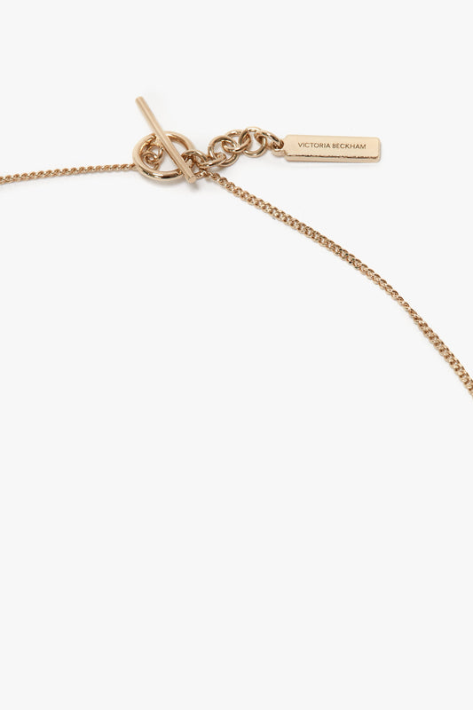 A close-up of a Victoria Beckham Exclusive Resin Pendant Necklace In Light Gold-White featuring a delicate chain, a T-bar closure, and a rectangular pendant engraved with "Victoria Beckham.