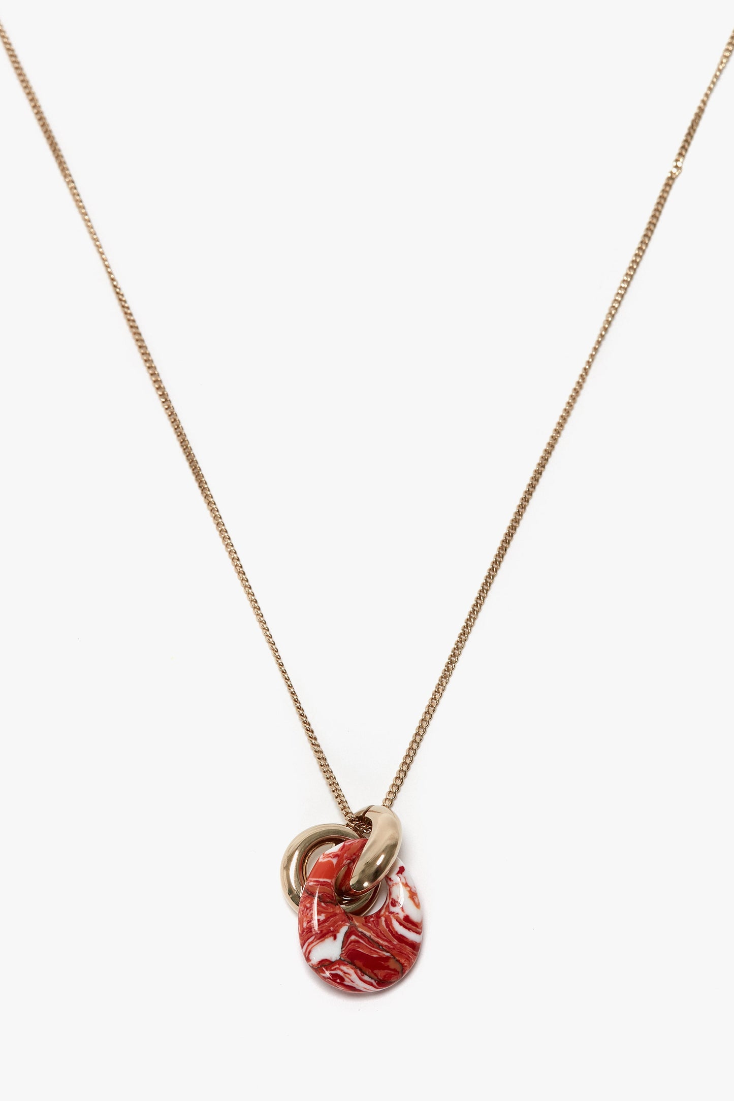 Victoria Beckham's Exclusive Resin Pendant Necklace in Light Gold-Orange features a light gold necklace with a resin pendant, showcasing a red and white marbled circular piece intertwined with a 100% brass ring.