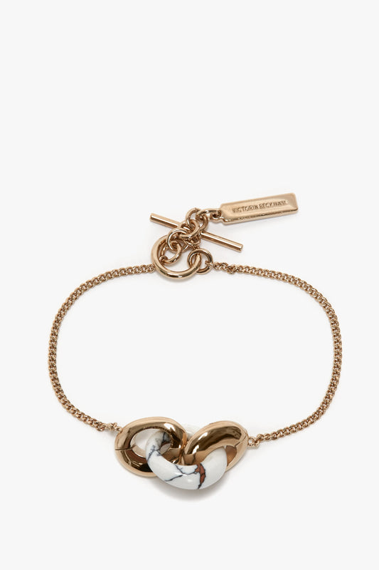 The Victoria Beckham Exclusive Resin Charm Bracelet In Light Gold-White features a marble-patterned knot centerpiece and a toggle clasp, crafted from 100% brass.