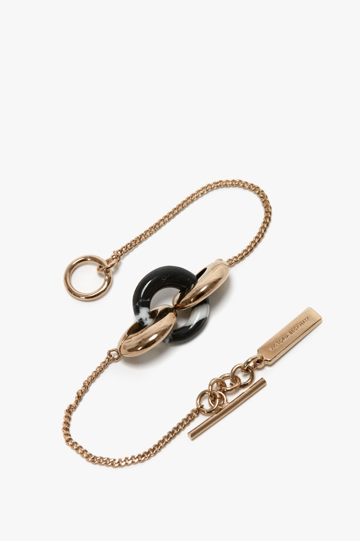 Victoria Beckham Exclusive Resin Charm Bracelet In Light Gold-Black with an interlocked black and white ring centerpiece and a rectangular tag engraved with text, crafted from 100% brass.