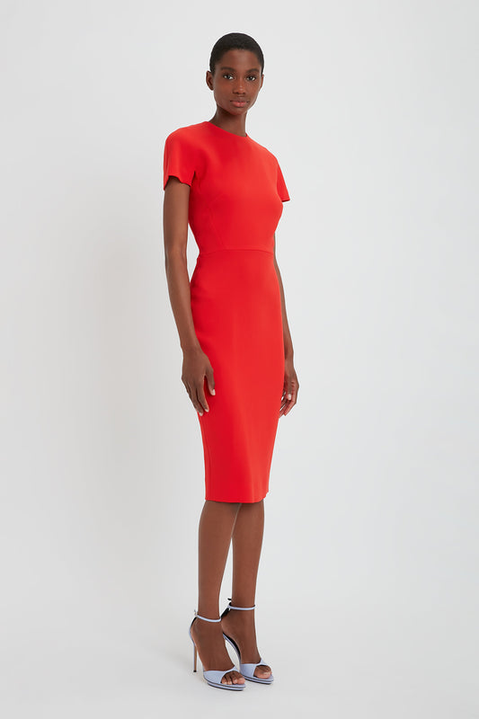 A black woman in a Victoria Beckham bright red, knee-length fitted T-shirt dress with short sleeves and pointy toe stiletto sandals, standing against a plain white background.