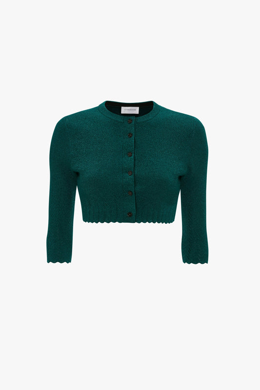 A green cropped cardigan with long sleeves, a round neck, and front button closure. The hem and cuffs have a scalloped edge design, enhanced by delicate pointelle stitch detailing that adds an extra touch of elegance. This is the VB Body Cropped Cardi In Lurex Green from Victoria Beckham.