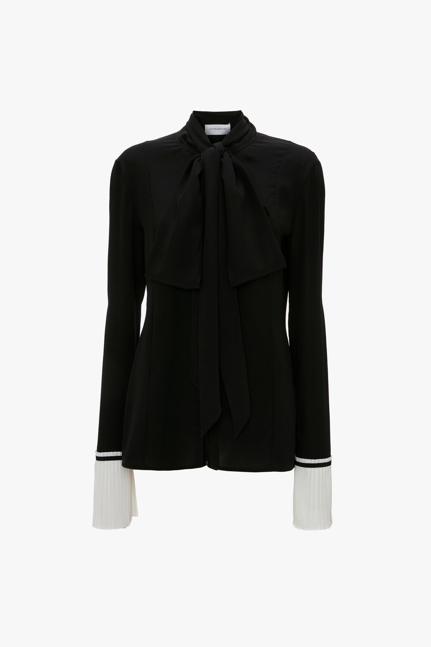 Pleat Cuff Blouse In Black by Victoria Beckham with long sleeves, a tie neck detail at the collar, and knife pleat white cuffs with striped detailing. 100% silk blouse that exudes elegance.