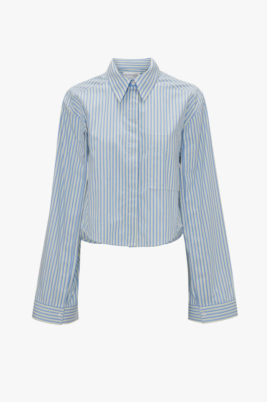 A cropped, long-sleeve, button-up shirt with light blue and white vertical stripes, combining masculine tailoring with a feminine silhouette for versatile styling. The Button Detail Cropped Shirt In Chamomile Blue Stripe by Victoria Beckham.
