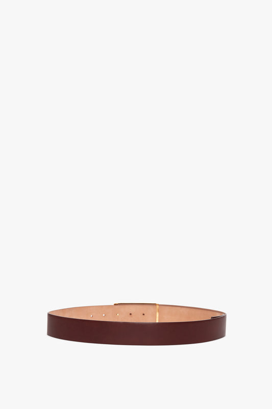 A smooth calf leather belt with gold hardware, it features a gold-colored buckle and lies flat against a white background. The belt, Jumbo Frame Belt In Burgundy Leather by Victoria Beckham, adds a touch of elegance to any outfit.