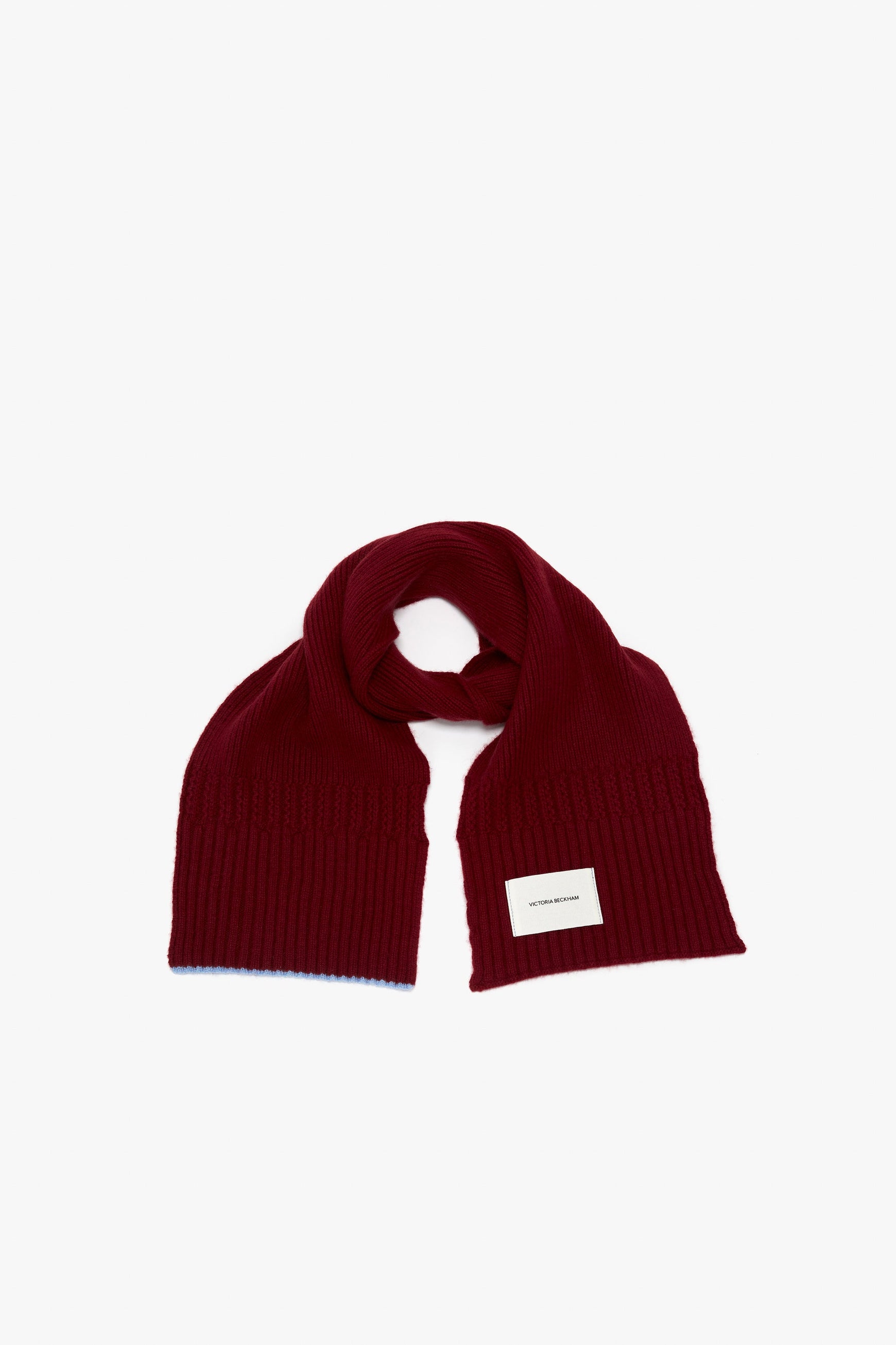 A red knitted luxury scarf with a small Victoria Beckham logo label, displayed flat on a white background.