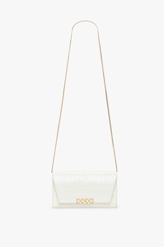 A white, rectangular Exclusive Wallet On Chain In Ivory Croc-Effect Leather by Victoria Beckham with a gold clasp and a long, thin gold chain strap is displayed against a plain white background.