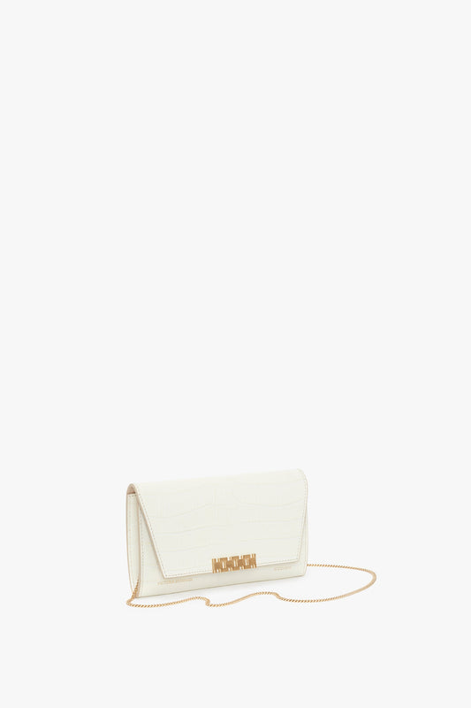 A white clutch purse with a textured finish, gold-tone chain strap, and gold hardware accent on the flap closure. This elegant accessory, the Exclusive Wallet On Chain In Ivory Croc-Effect Leather by Victoria Beckham, features embossed croc leather for added sophistication.
