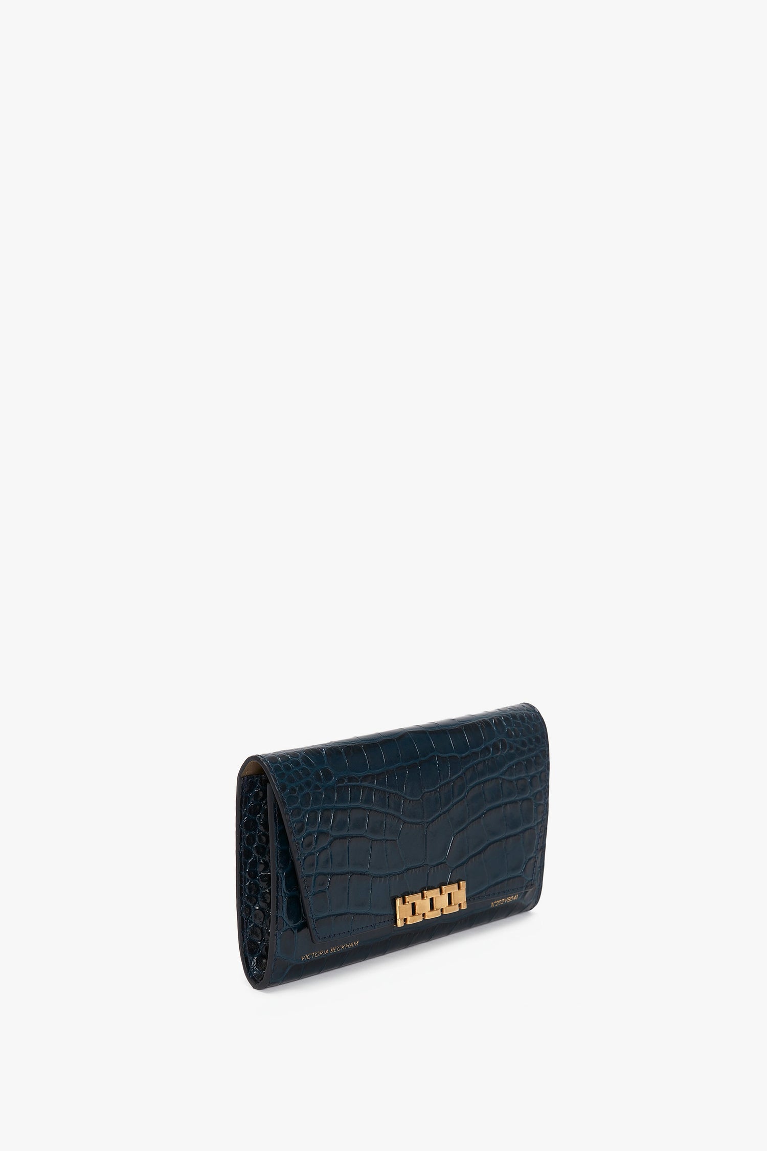 A dark teal, crocodile-patterned leather Wallet On Chain In Midnight Croc-Effect Leather clutch by Victoria Beckham with a gold clasp, viewed from a slight angle on a white background.