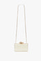 A small white rectangular Frame Flower Minaudiere in Bag Chamomile with a long gold chain strap and a floral embellishment on top, this accessory channels the chic elegance of Victoria Beckham.