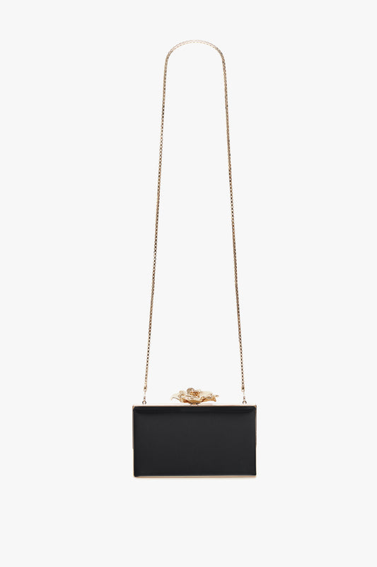 A black rectangular clutch bag with a brass Frame Flower Minaudiere frame and a decorative golden frog on top, isolated on a white background by Victoria Beckham.