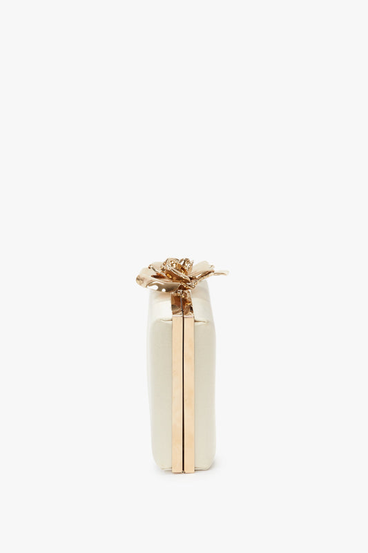 Side view of a compact, white Frame Flower Minaudiere in Chamomile by Victoria Beckham with gold accents, a flower-shaped clasp on the top, and a bespoke brass frame.