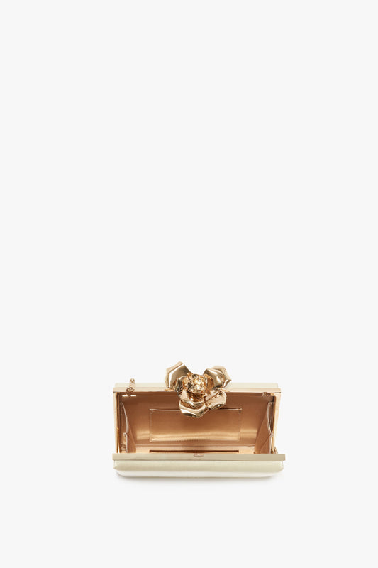 Small, open, rectangular metallic clutch with a bespoke brass frame and a decorative flower clasp on top. The interior is lined with beige fabric, embodying the elegance of Victoria Beckham accessories. This is the Frame Flower Minaudiere in Chamomile by Victoria Beckham.