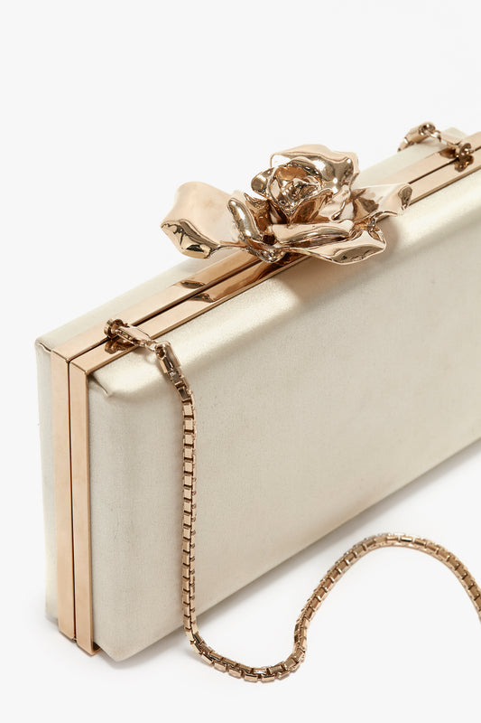 A rectangular beige clutch with a gold metal rose detail on the clasp, a bespoke brass frame, and a gold chain strap, the Victoria Beckham Frame Flower Minaudiere in Chamomile.