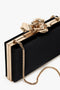 Frame Flower Minaudiere Bag in Black by Victoria Beckham with gold trim, featuring an exquisite flower clasp and a bespoke brass frame, complemented by a gold chain strap.