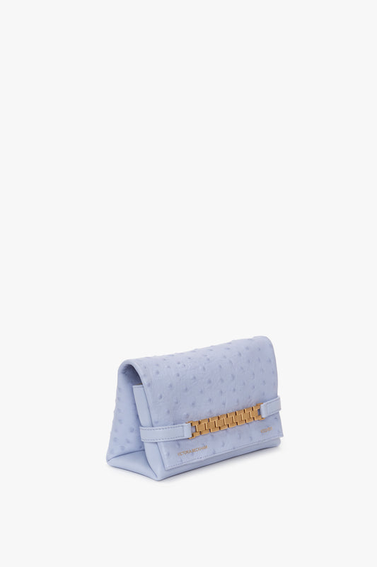 A light blue, textured Mini Chain Pouch With Long Strap In Frost Ostrich-Effect Leather with a gold rectangular clasp, featuring embossed leather details by Victoria Beckham.