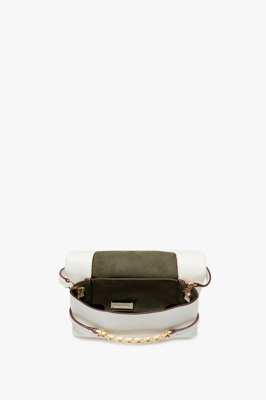 A small, open satchel-style handbag with a white exterior, green suede flap, and gold-tone chain accents. Inspired by Victoria Beckham's Mini Chain Pouch Bag With Long Strap In White Leather, it boasts a single compartment and a small pocket inside. The addition of a removable strap adds versatility to this chic accessory.