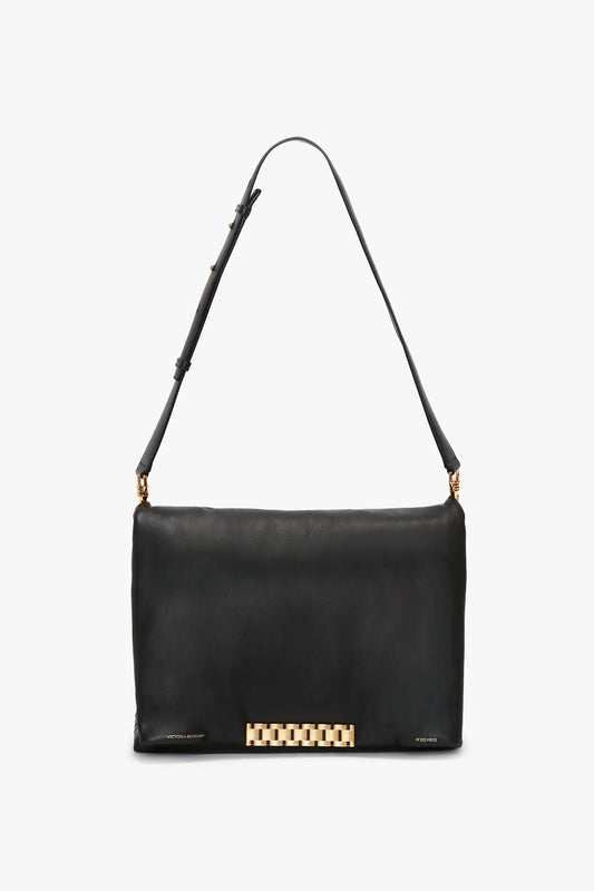 A Puffy Jumbo Chain Pouch In Black Leather by Victoria Beckham, featuring a single adjustable shoulder strap and a gold rectangular decorative clasp at the front center.