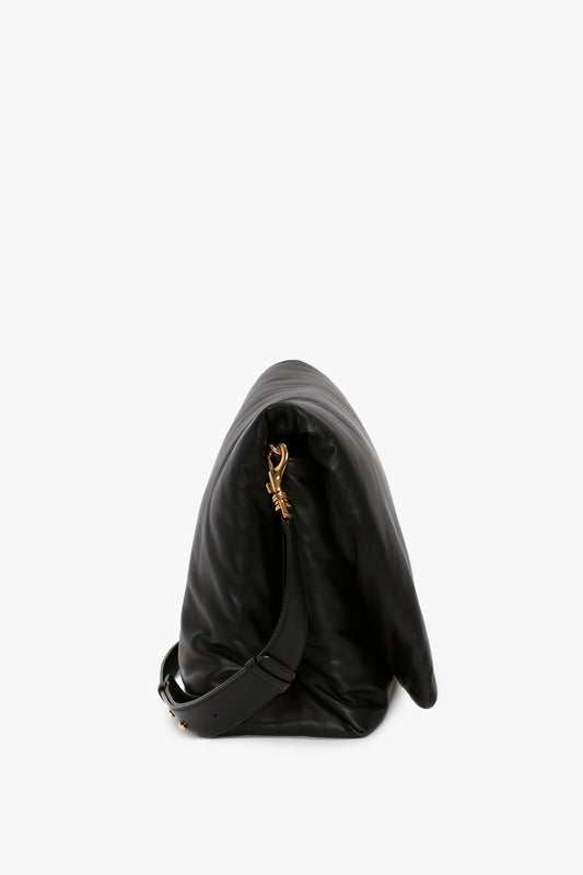 Side view of a Victoria Beckham Puffy Jumbo Chain Pouch In Black Leather with a gold clasp and an adjustable shoulder strap lying against a white background.