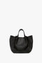 A W11 Medium Tote Bag In Black Leather by Victoria Beckham in luxurious grained leather, featuring short handles and gold text branding at the bottom, perfect for versatile styling.