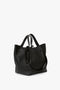 W11 Medium Tote Bag In Black Leather with two sets of handles, one shorter and one longer, made from luxurious grained leather, resting on a flat surface. Perfect for versatile styling. By Victoria Beckham.