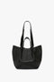 A W11 Medium Tote Bag In Black Leather by Victoria Beckham, made from luxurious grained leather, with wide, long straps and an open top, perfect for versatile styling. Displayed on a plain white background.