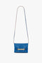 A sapphire blue leather shoulder bag with a long strap and a gold chain detail on the front, resembling a chic Mini Chain Pouch Bag With Long Strap In Sapphire Blue from Victoria Beckham.