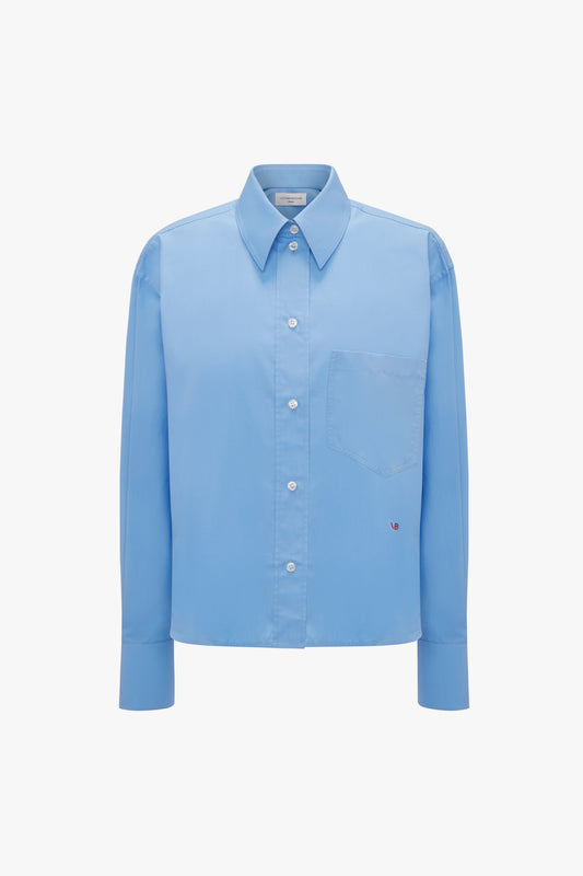 A Cropped Long Sleeve Shirt In Oxford Blue by Victoria Beckham with long sleeves, a front pocket, and a relaxed fit.