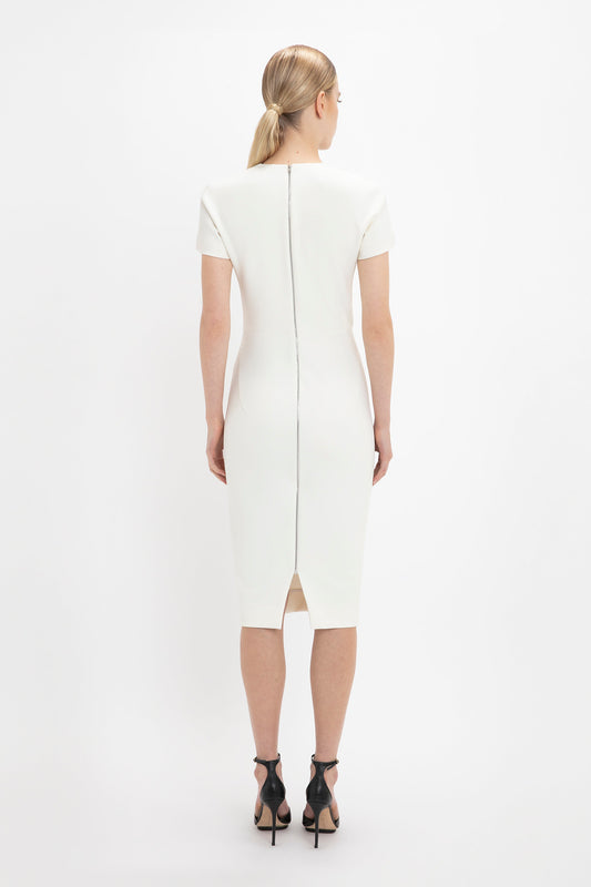 A woman wearing a Victoria Beckham ivory knee-length fitted T-shirt dress with short sleeves and a back zipper, viewed from behind, standing against a white background.