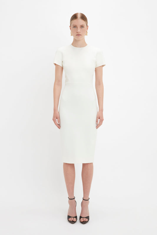A woman in a simple, elegant Victoria Beckham ivory fitted t-shirt dress and black pointy toe stiletto sandals, standing against a plain white background.