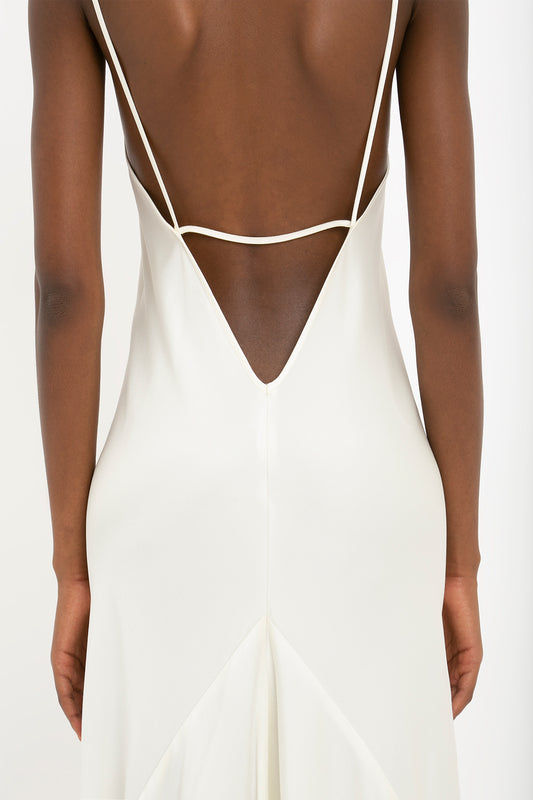 A back view of a person wearing the Victoria Beckham Floor-Length Cami Dress In Ivory with thin straps, showing smooth skin and elegant crepe back satin details, reminiscent of 90s fashion.