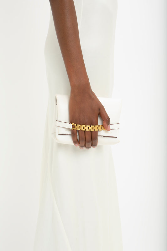 A person in a Victoria Beckham Floor-Length Cami Dress In Ivory is holding a white clutch with a gold chain detail on the handle, evoking a timeless 90s fashion vibe.