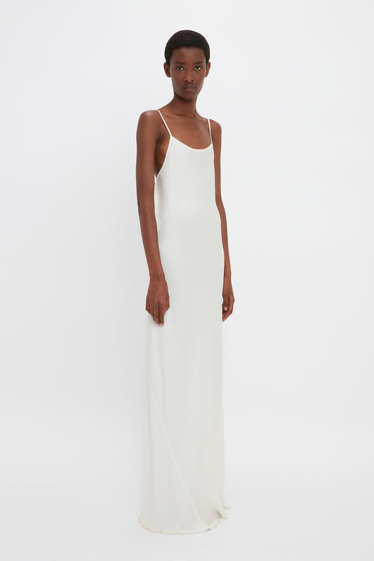 A person wearing a Victoria Beckham Floor-Length Cami Dress In Ivory stands against a plain white background, channeling 90s fashion.