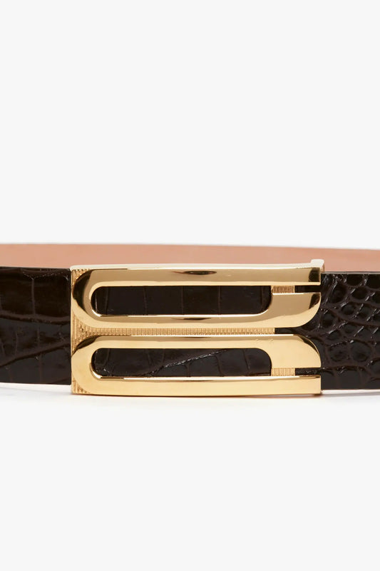 A black croc-effect leather belt with a gold-tone frame buckle, featuring a crocodile-textured design and contemporary styling has been replaced by the Jumbo Frame Belt In Chocolate Croc-Effect Leather from Victoria Beckham.