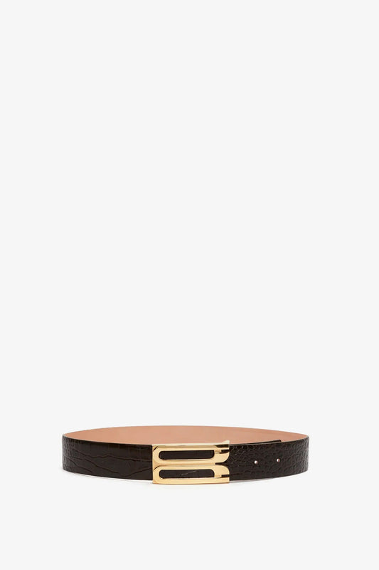 A dark brown croc-effect leather belt with a gold-toned rectangular frame buckle, showcasing contemporary styling on a white background. Presenting the **Jumbo Frame Belt In Chocolate Croc-Effect Leather** by **Victoria Beckham**.