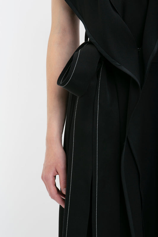 Close-up of a person wearing a Victoria Beckham Trench Dress In Black with white stitching detail and a bow on the side. The person's left arm is visible.