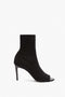 A single black, open-toe high-heeled ankle boot crafted from elegant tight-fit black knit fabric against a white background -- the Sunday 90Mm Knitted Open Toe Ankle Boot by Victoria Beckham.