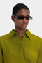 Person wearing Victoria Beckham Mini Visor Sunglasses In Black-Green and a green collared shirt with a chest pocket, sporting a futuristic aesthetic.