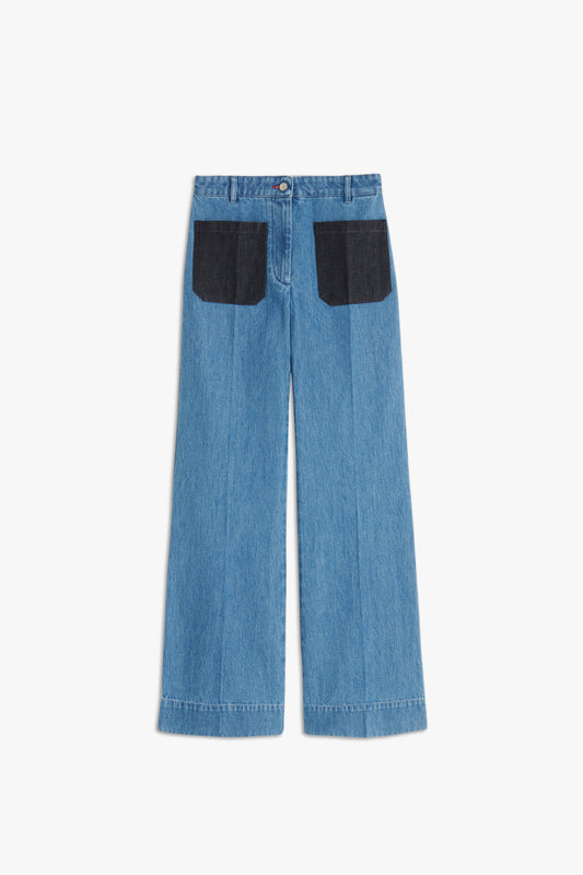 The Victoria Beckham Alina High Waisted Patch Pocket Jean In 70s Wash features high-waisted wide-leg blue denim trousers with black back pockets, button and zipper closure, stitched seams, and a vintage 70s wash.