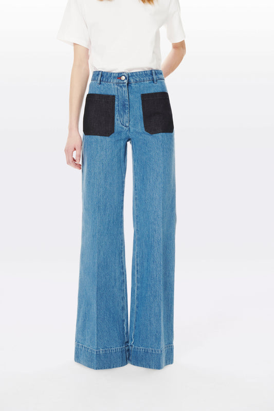 A person wearing a white top and blue Victoria Beckham Alina High Waisted Patch Pocket Jean In 70s Wash.