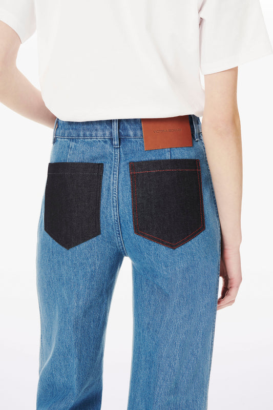 Back view of a person wearing Victoria Beckham Alina High Waisted Patch Pocket Jean In 70s Wash with black back pockets and a white T-shirt. A brown leather patch is on the waistband.