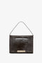 A black, crocodile-patterned leather Jumbo Chain Pouch Bag In Chocolate Croc-Effect Leather by Victoria Beckham with a short strap and a gold-colored clasp at the front.