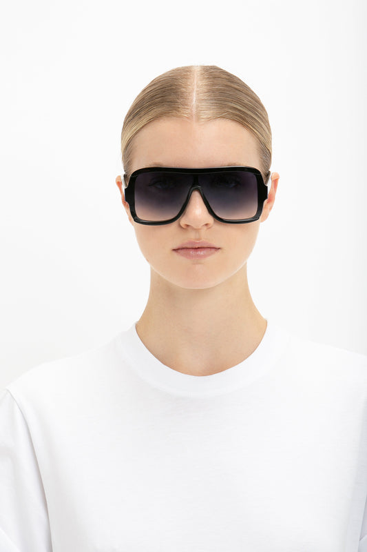 A woman with slicked-back hair wearing Victoria Beckham's Layered Mask Sunglasses in Black Gradient and a white t-shirt against a white background.