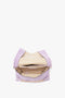 Open Victoria Beckham Chain Pouch Bag with Strap in Lilac Suede with a beige interior, showing an inner zippered pocket, small label, and gold chain detail on the edge. Crafted from Italian leather, it features a detachable strap for versatility.