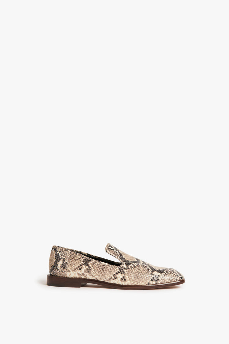 The Victoria Beckham Hanna Loafer in Beige Snake Print, featuring a beige snake print, showcases a classic loafer design with a flat brown sole, viewed from the side against a white background.