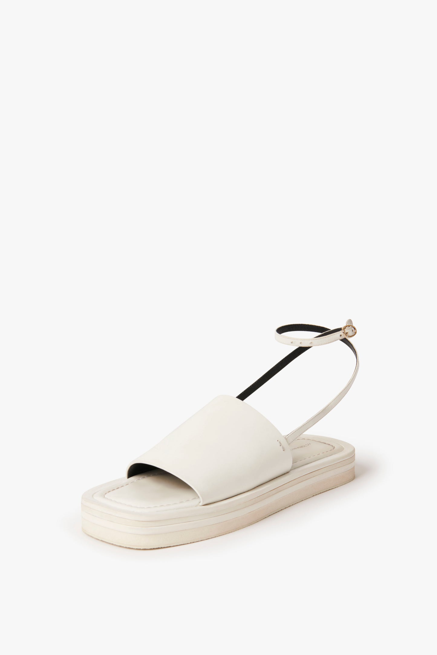 The Victoria Beckham Frances Sandal in White features a white open-toe design with a thick sole, wide front strap, and black ankle strap with a small buckle. This chunky sandal boasts a minimalist style reminiscent of 90s aesthetic.